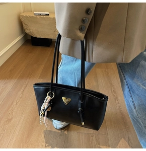 Détail du sac à bandoulière en simili cuir noir avec logo métal et pompon tissé