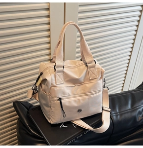 Detail of a beige nylon tote bag with front zipper pocket on a studio background