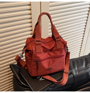 Detail view of brick red nylon tote bag featuring multiple zipper pockets and fabric straps