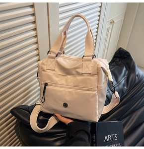 Detail of beige nylon tote bag featuring front zip pocket and durable webbing handles