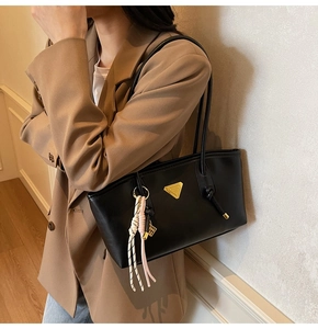 Détail du sac bandoulière noir avec logo triangle doré et pendentif tressé rose