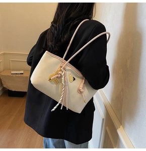 Détail du sac crème avec bordure rose, logo en triangle et gland porté par le modèle