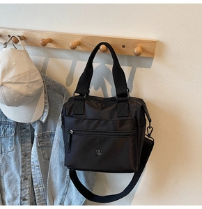 Detail of black nylon tote bag with metal M logo and zipper pocket on wooden hook
