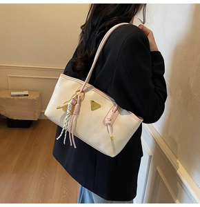Détail du sac cabas beige avec bordure rose, logo doré et pendentifs à pompons