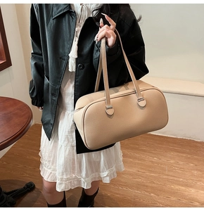 Model wearing a beige lychee leather boston bag with silver hardware and shoulder strap