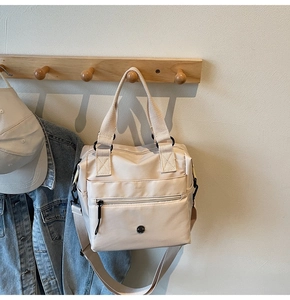 Detail of white nylon tote bag showing wide straps and front zip pocket on hook