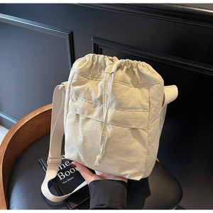 Dettaglio borsa a secchiello in nylon crema con chiusura a coulisse e tracolla