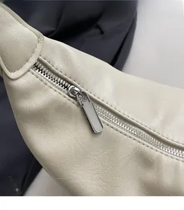 Close-up of smooth silver metal zipper on cream-colored textured leather shoulder bag
