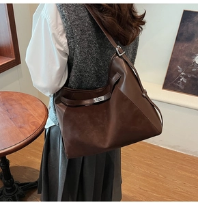 Detail of dark brown leather tote bag with silver buckle worn on shoulder in a cozy room