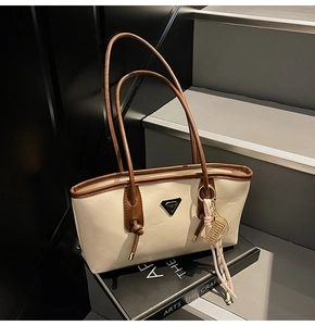 Détail du sac fourre-tout crème avec bordure marron et breloque abaque dorée à pompon