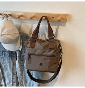 Detail of dark brown nylon tote bag with metal logo and zipper on a wooden hanger