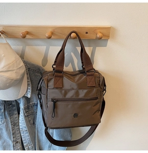Detail view of coffee nylon tote bag with round metal logo and zipper pocket on wood hook