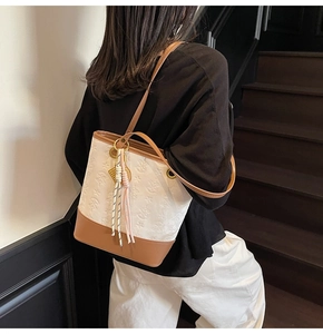 Detail view of contrast bucket bag with embossed texture and tassel charm detail