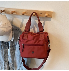 Detailed view of red nylon tote bag with metal logo hanging on a wooden hook