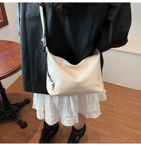 Détail d'un sac hobo en cuir blanc crème avec pendentif cœur argenté et fine bandoulière