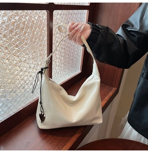 Détail d'un sac hobo blanc brillant avec pendentif coeur sur fond de lumière douce
