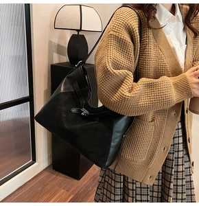Detail of a black leather tote bag with decorative belt buckle held by a model