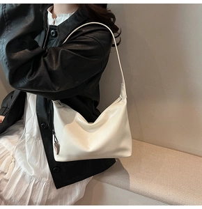 Détail d'un sac sous le bras blanc crème avec un pendentif cœur argenté et cuir souple