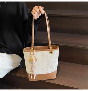 Close-up detail of white bucket bag with star embossing and woven tassels on brown strap