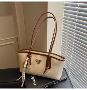 Détail du sac crème avec anses marron, badge triangle en métal et foulard en soie