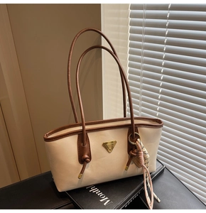 Détail du sac à bandoulière crème avec bordure marron et logo triangulaire sur mur texturé