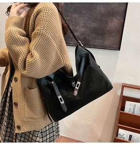 Detail of a black leather and suede tote bag with silver square buckle shown on shoulder