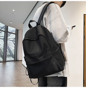 Minimalist black nylon backpack shown from a side-rear angle on a person for daily commute