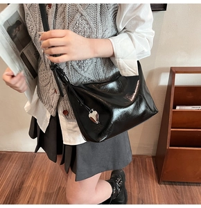 Détail du sac à bandoulière noir brillant avec un pendentif cœur argenté au style rétro