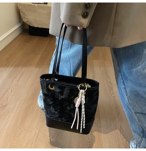 Fashionable black tote bag with tennis racket charm worn on shoulder in a cozy interior