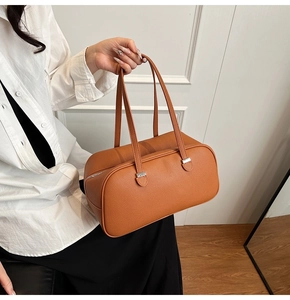 Close-up of brown litchi pattern leather handbag held by a model in a minimal setting