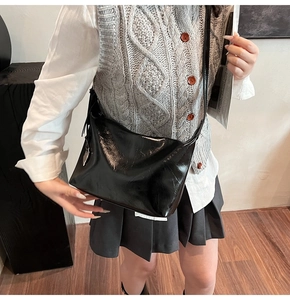 Sac à bandoulière hobo noir brillant porté par un mannequin pour un look tendance