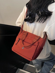 Red-brown nylon tote bag with adjustable strap shown from a side-rear perspective