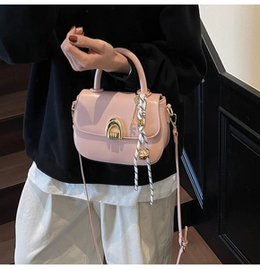 Detail of light pink saddle bag with golden U-buckle, handle ribbon and golden ball charm