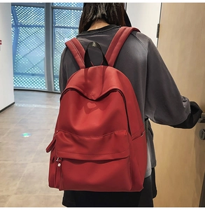 Detail of red water-resistant nylon backpack featuring large front pocket and side bottle pouch