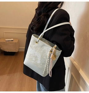 Detail of light blue embossed bucket bag with gold charms shown on model shoulder