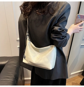 Vue détaillée du sac hobo crème brillant avec breloque cœur argentée porté à l'épaule