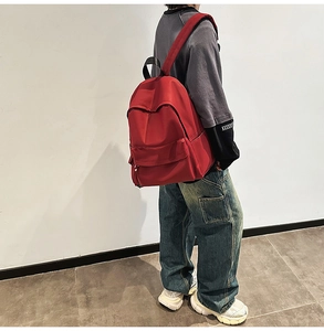 Side view of a minimalist red waterproof backpack being worn by a model in a studio