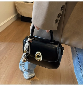 Detail of black leather saddle bag with gold U-shaped buckle and striped handle rope