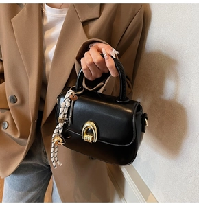 Detail of a vintage black saddle bag featuring a gold arch lock and woven rope charm