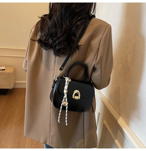 Detail of black saddle bag featuring golden horseshoe buckle and decorative silk scarf