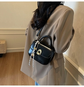 Detail of black saddle bag with golden horseshoe buckle and striped silk scarf wrap