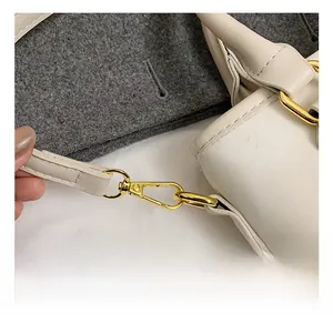 Detail of premium gold-tone metal hook and textured cream leather strap on bucket bag