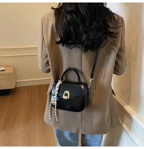 Rear view of model wearing black leather saddle bag with gold buckle and striped tassel