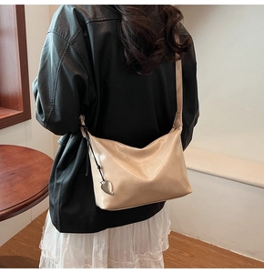 Détail du sac beige en forme de croissant avec pendentif coeur et large bandoulière