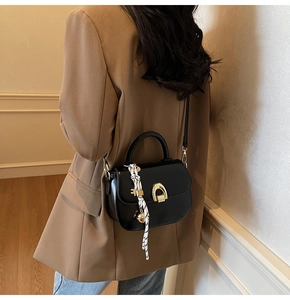 Detail of black saddle bag with golden horseshoe clasp and patterned silk scarf handle