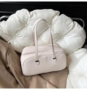 Close-up of cream white Boston bag with litchi texture on a cloud-shaped cushion