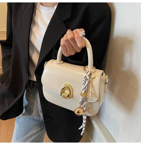 Detail of cream saddle bag featuring gold horseshoe buckle and woven key charm