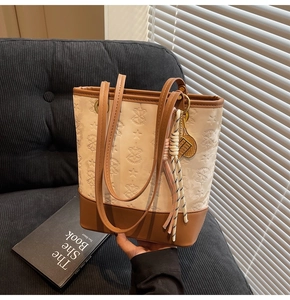 Detail of a cream and brown tote bag with embossed star patterns and a tennis racket charm