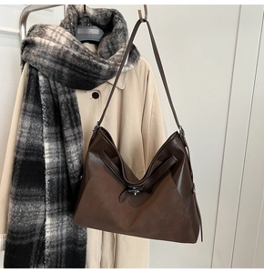 Detail of dark brown leather tote bag paired with an autumn trench coat and plaid scarf