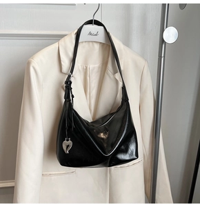 Gros plan du sac hobo noir brillant avec pendentif cœur sur un costume blanc